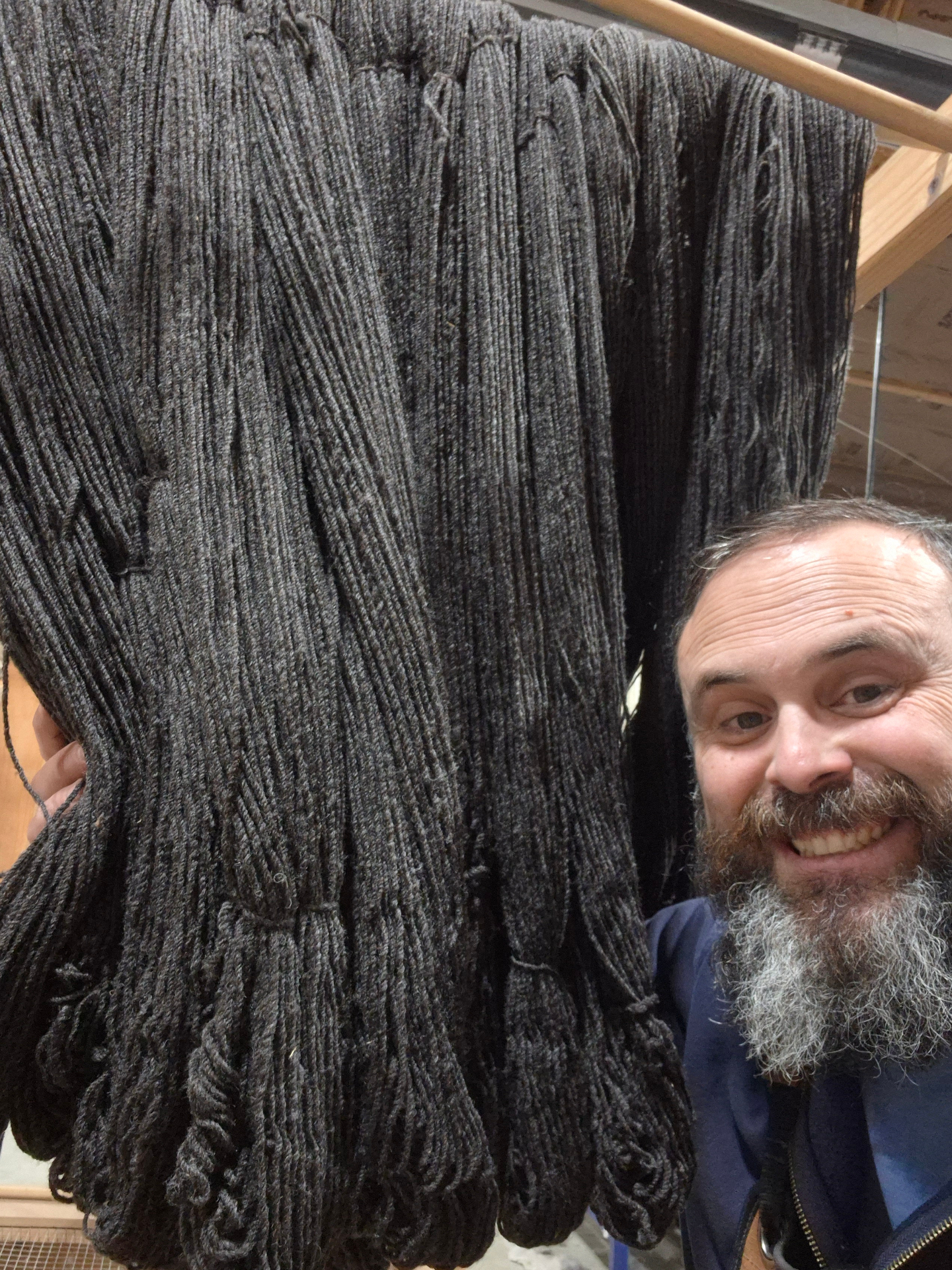 Isaac holding a rack of finished dark gray skeins at the mill